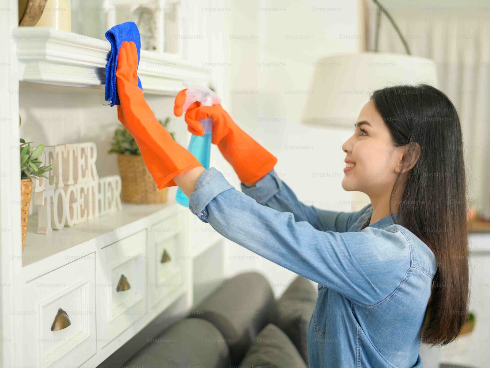 Woman cleaning a shelf with a spray bottle in a living room